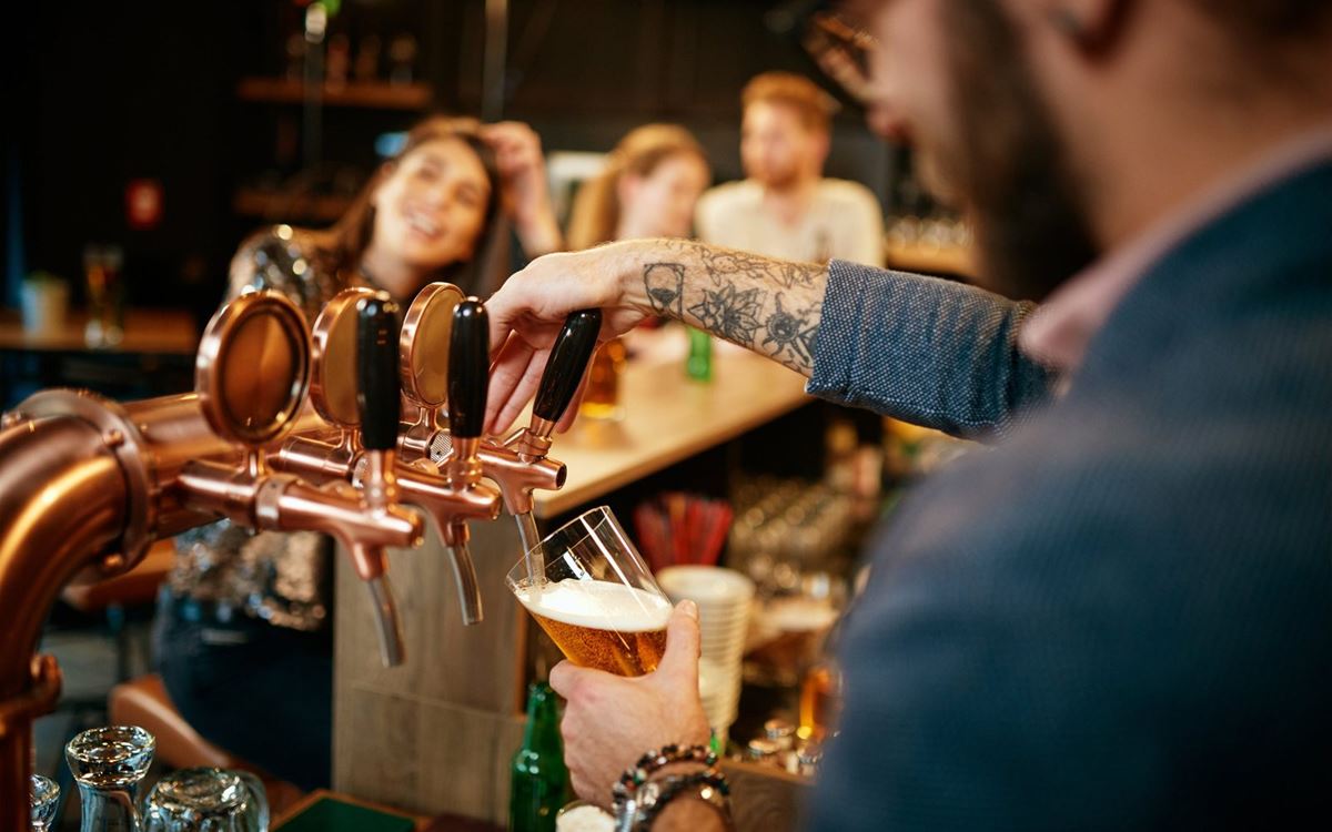 Bartender pouring a pint at a busy pub bar